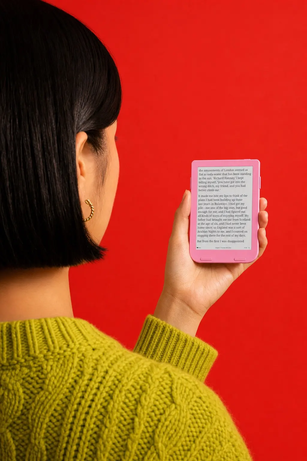 Over the shoulder of a woman in a green sweater reading a pink Snug Mini